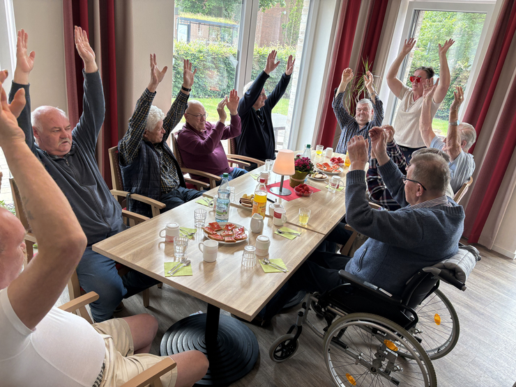 Alle sitzen um den Tisch und schlagen Arme hoch